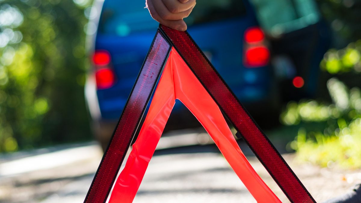 Hand placing an emergency warning triangle on the road beside a vehicle