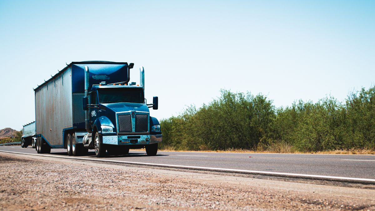 Blue semi-truck driving on an open rural highway under clear skies