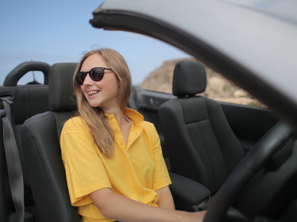 Mujer sonriente manejando un convertible por una carretera costera